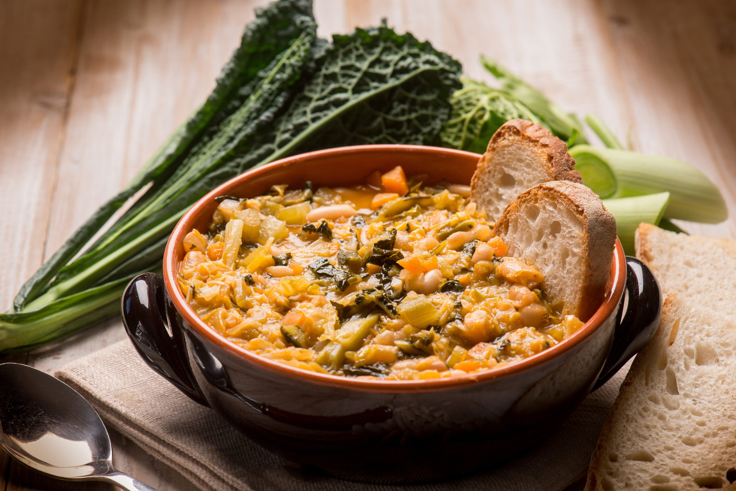 Close up of ribollita traditional tuscan soup, arranged on a wooden counter with fresh greens in the background