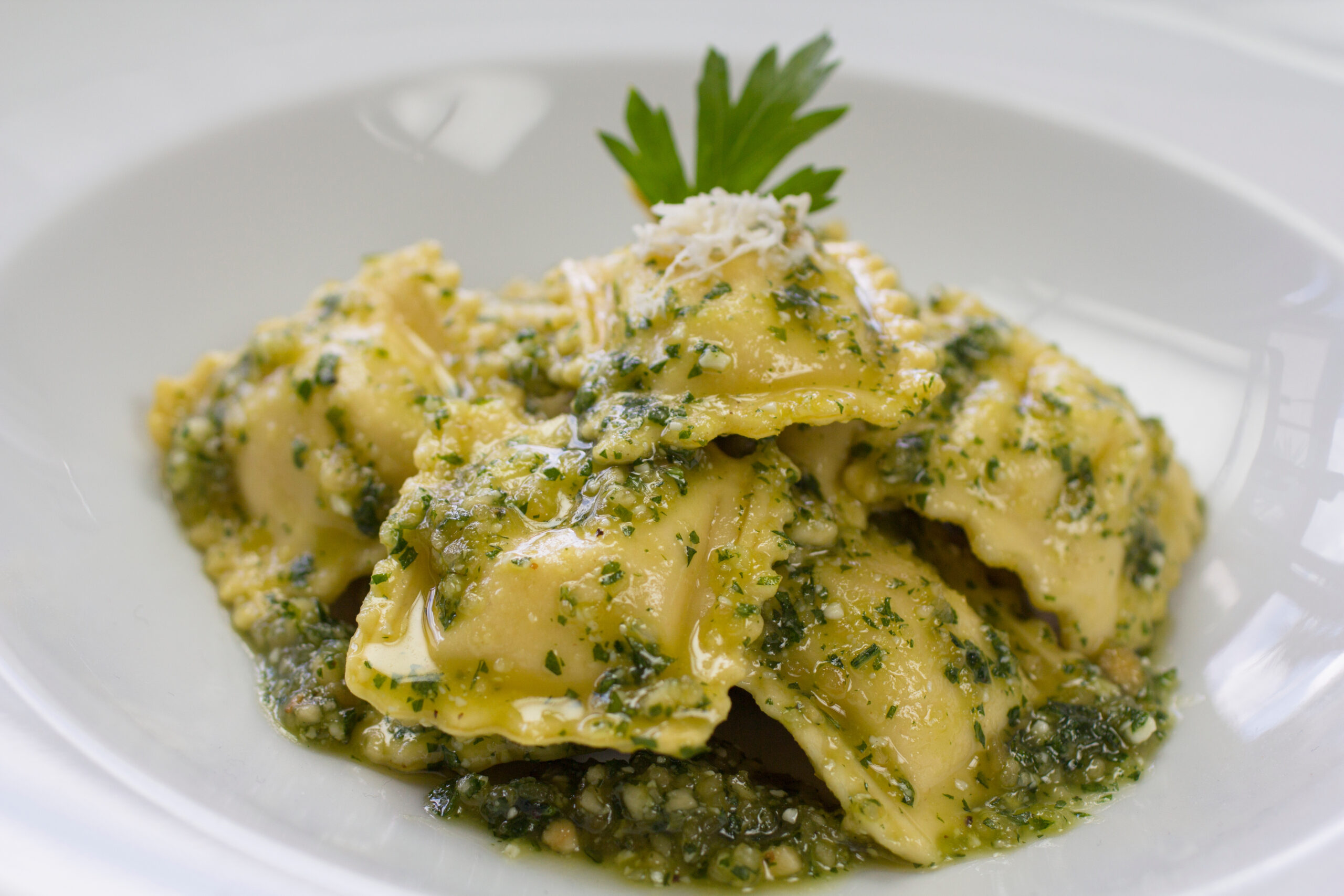 A plate of ravioli dressed with fresh pesto in a white bowl