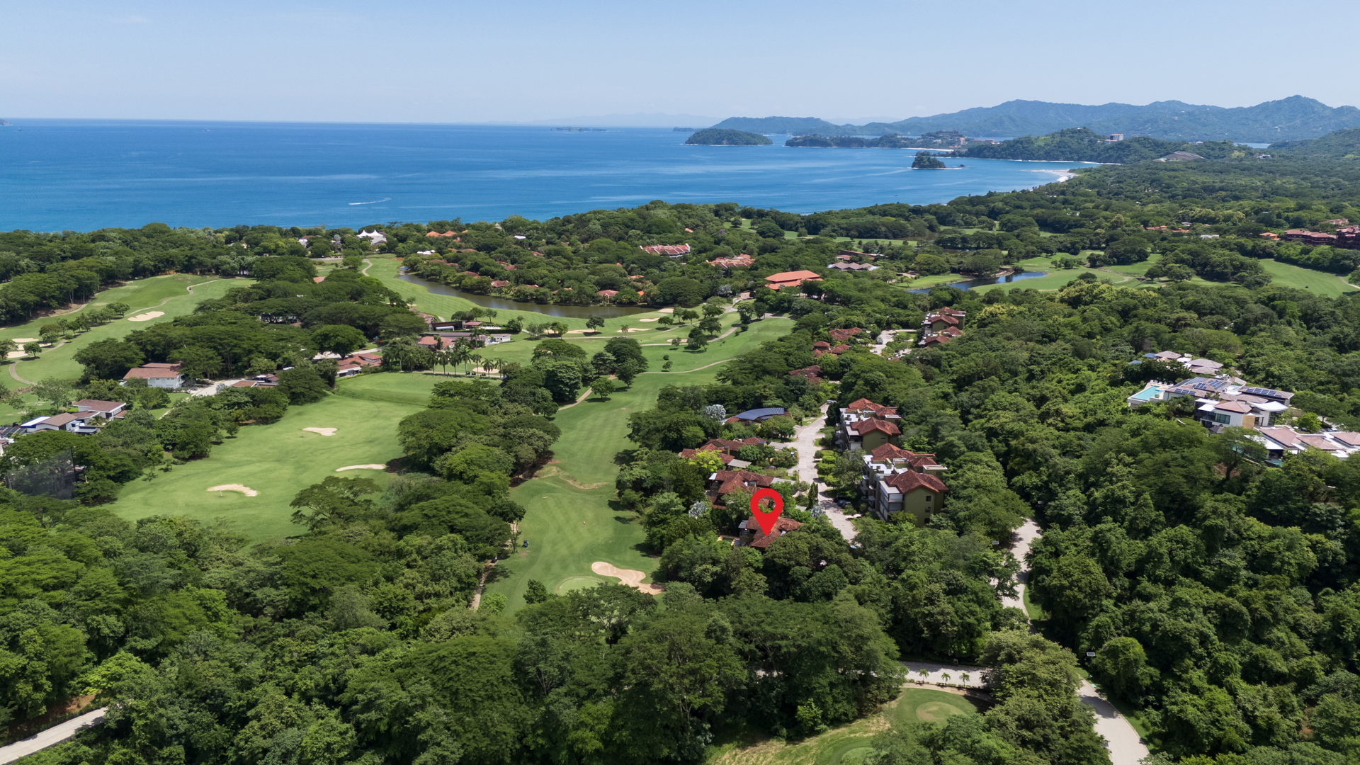 Aerial view of Villa Conchal showing a curving shoreline with a mix of grasslands and tress, and deep blue water beyond