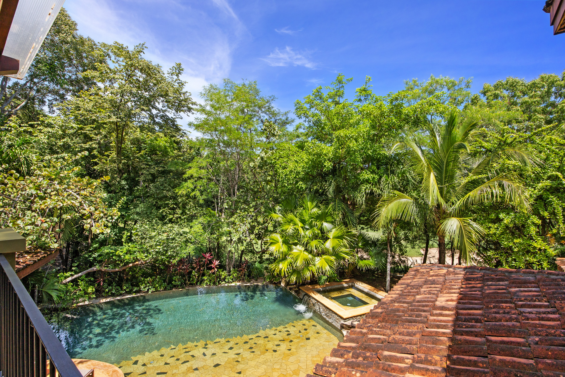 View of the pool and its surrounding lush greenery from an upstairs balcony at Villa Conchal